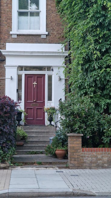 A close-up view of a residential garden entrance showing a red front door with a brass letterbox and a brass door knocker, set within a white decorative porch surround featuring classic molding and a 